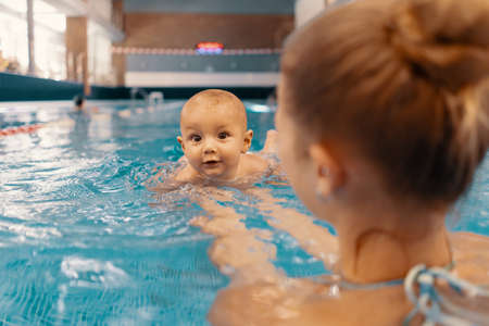 Young mother and her baby enjoying a baby swimming lesson in the pool. Child having fun in water with momの写真素材