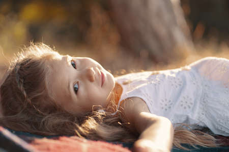 Carefree lovely girl in white dress with blonde wavy hair lying on a blanket enjoying the sun raysの写真素材