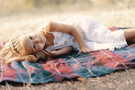 Carefree lovely girl in white dress with blonde wavy hair lying on a blanket enjoying the sun raysの写真素材