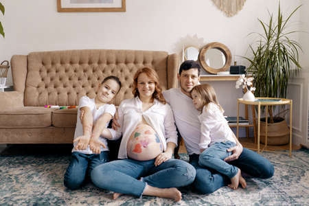 Happy family portrait at home. Parents, pregnant mother and father with lovely two kids sit on the...