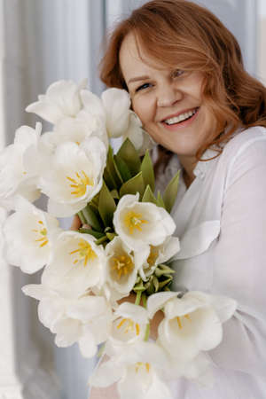 Close up portrait pretty pregnant lady with white tulips at home thinking about her motherhood