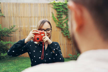 Young couple in love taking a selfie with an instant camera. Lying on the grass in the yard of his...