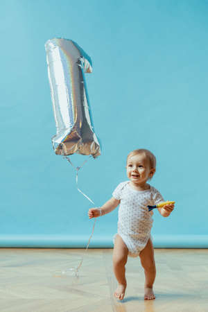 Funny kid running happy with one year balloon on blue background. First birthday celebration copy spaceの写真素材