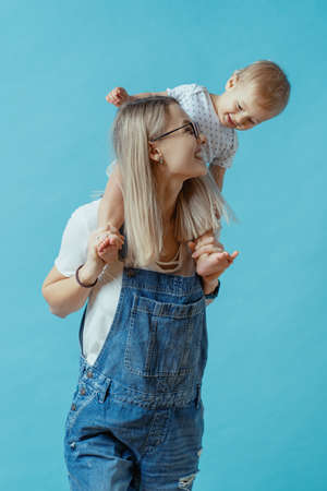 Cheerful young mom posing with her one year kid on blue backgroundの写真素材