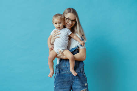 Cheerful young mom posing with her one year kid on blue background