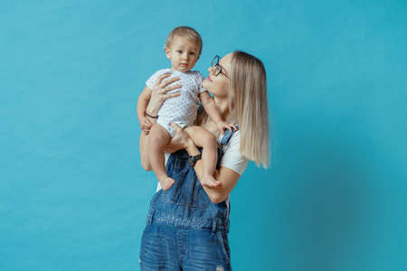 Cheerful young mom posing with her one year kid on blue backgroundの写真素材
