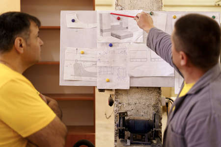 Two colleagues carpenters discussing and working with a technical blueprint drawing construction...