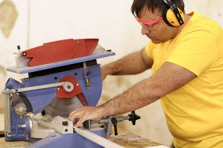 Carpenter cutting a piece of wood for furniture in his woodwork workshop, using a circular saw, and...