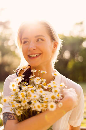 Portrait of a Sunny woman embracing a bunch of chamomile with the sun rays on her face enjoying lifeの写真素材