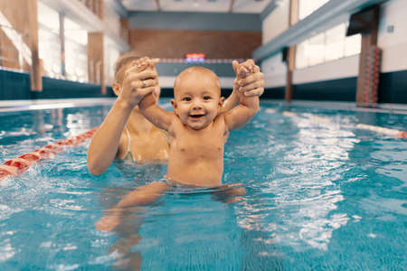 Young mother and her baby enjoying a baby swimming lesson in the pool. Child having fun in water...