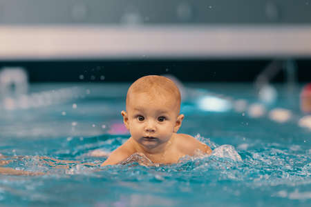 Young mother and her baby enjoying a baby swimming lesson in the pool. Child having fun in water with momの写真素材