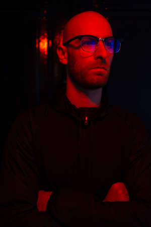 Close up portrait of hairless man wearing glasses, beard with red neon light reflected on his face...