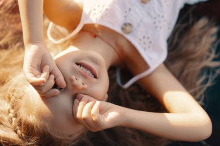Carefree lovely girl in white dress with blonde wavy hair lying on a blanket enjoying the sun raysの写真素材