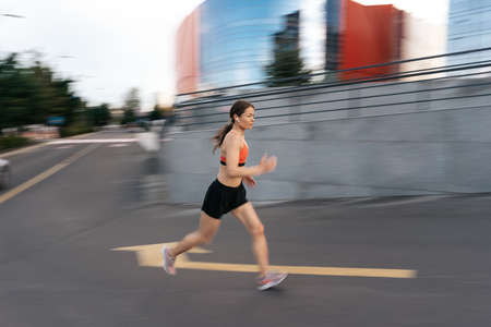 Young woman sprinting in the morning outdoors. Side view of female runner in motion working out in the city.の写真素材