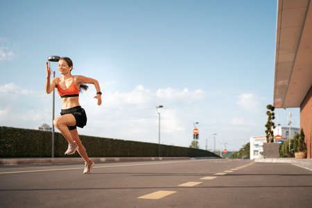 Young woman sprinting in the morning outdoors. Side view of female runner working out in the city...