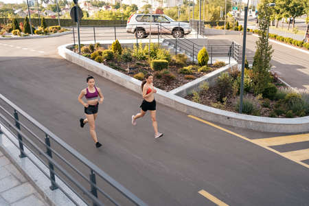 Young woman running on sidewalk in morning. Health conscious concept. Healthy active lifestyle. Active girls jogging together on road in the city.の写真素材