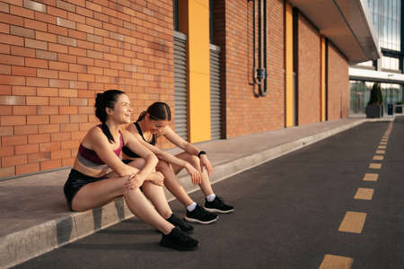 Two women before urban workout. Girls preparing for running and sitting in the street. Fitness breakの写真素材