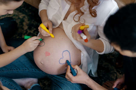 Lovely family hands drawing hearts on moms tummy expecting a new baby to come in their happy life.の写真素材