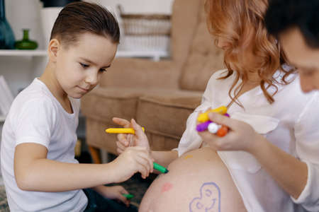 Lovely family drawing hearts on moms tummy expecting a new baby to come in their happy life.の写真素材