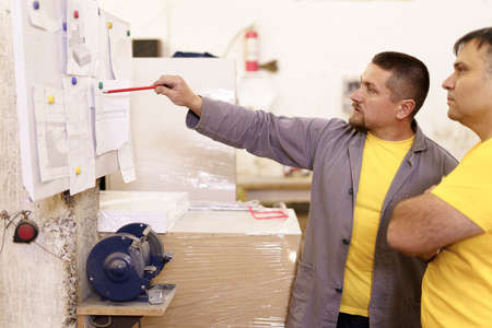 Two colleagues carpenters discussing and working with a technical blueprint drawing construction...
