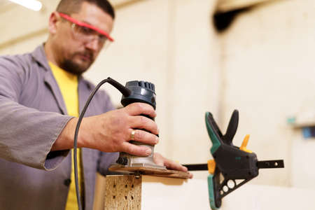Carpenter sanding a wood with sander wearing safety goggles in his workshop. Man loves his job.
