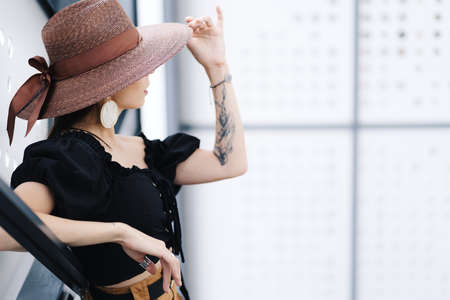 Fashionable brunette woman with long hair, wearing stylish large wicker hat, posing on the stairs....