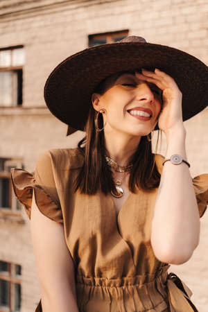 Young fashion girl dressed in a summer dress with a wicker wide hat walks and poses in the old city....