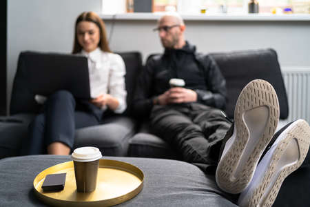 Young Woman and Young Man Working on the Notebook, Drinking Coffee and Sitting on the gray Sofa in...