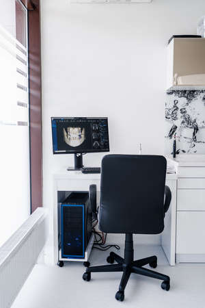 Interior of dental practice room with chair, lamp, dental scan on the display and stomatological...