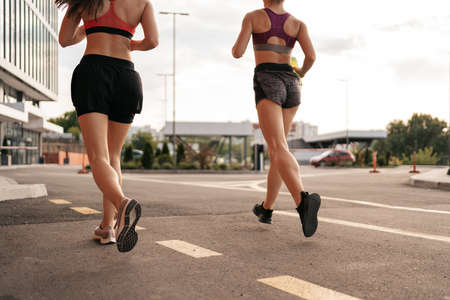 Young woman running on sidewalk in morning. Health conscious concept. Healthy active lifestyle. Active girls jogging together on road in the city.の写真素材