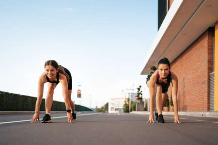 Sprinters starts out on racetrack with bright light. Low section shot of female athletes starting a race in on the road in the cityの写真素材