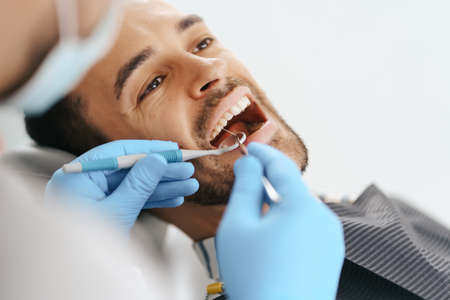 Smiling young man sitting in dentist chair while doctor examining his teethの写真素材