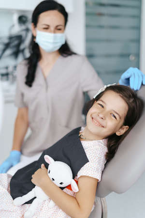 Cute little girl sitting on a modern dental chair and having dental consultation with dentistの写真素材