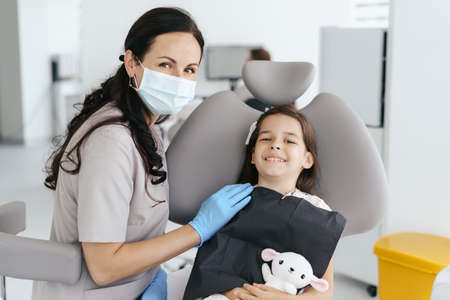 Cute little girl sitting on a modern dental chair and having dental consultation with dentistの写真素材