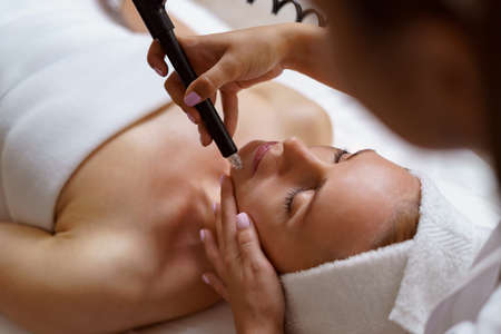 View of doctor cosmetologist doing anti aging procedure in cosmetology office. Satisfied woman in...