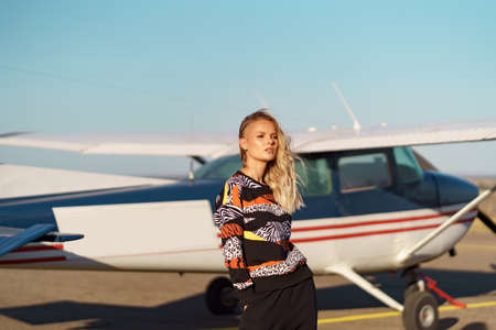Young woman model with a modern haircut and fashionable sunglasses posing near a red plane wearing trendy casual outfitの写真素材