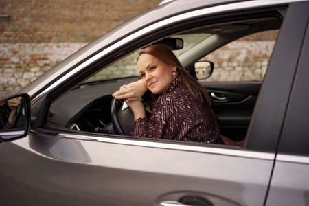 Smiling satisfied woman lying on an automobile steering wheel. Happy client of car dealership after...