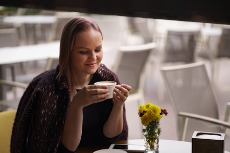 Close-up portrait of smiling woman drinking coffee alone. Lovable lady standing near window and...