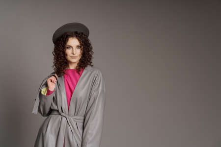 Studio shot of curly fashion model in bright pink clothes and leather jacket on gray background with...