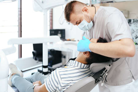 Smiling young man sitting in dentist chair while doctor examining his teeth