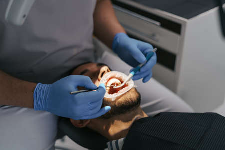 Young man sitting in dentist chair while doctor examining his teeth