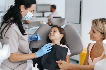 Cute little girl sitting on a modern dental chair and having dental consultation with dentistの写真素材