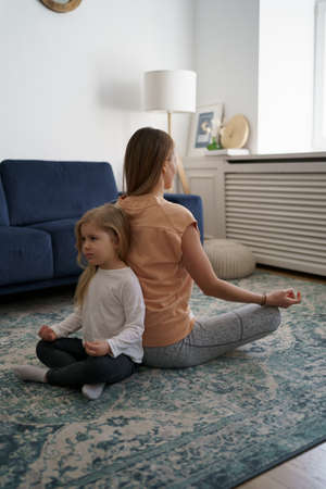 Young mother with little daughter practicing yoga at home. Family fizical activity, sporty mom and kidの写真素材