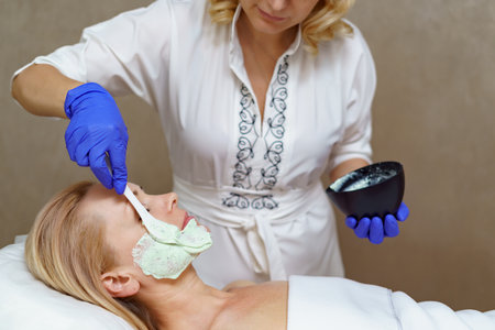 Hands of cosmetology specialist applying facial alginate mask using wooden spatula, making skin hydrated and face glowing and skin.の写真素材