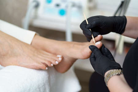 Specialist in beauty salon making french pedicure for female client. Relaxing at beauty salon, caring about nails.