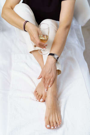 Manicure pedicure with glass with sparkling wine close up on white perfect shape hands spa salonの写真素材