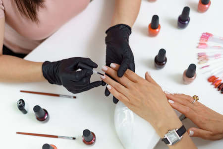Close up details of woman hands in black gloves making manicure in luxury beauty salon with modern equipment, soft colors, nail service, perfect client hands.の写真素材