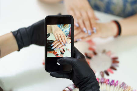 Manicurist takes a photograph of her work, beautiful woman manicure, with a smartphoneの写真素材
