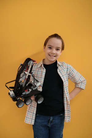 Smiling School boy holding a robot and its remote control on yellow wall backgroundの写真素材