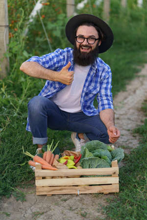 Farmer sits with a wooden box with fresh veggies in his garden smiling. Getting Ready for organic eco deliveryの写真素材